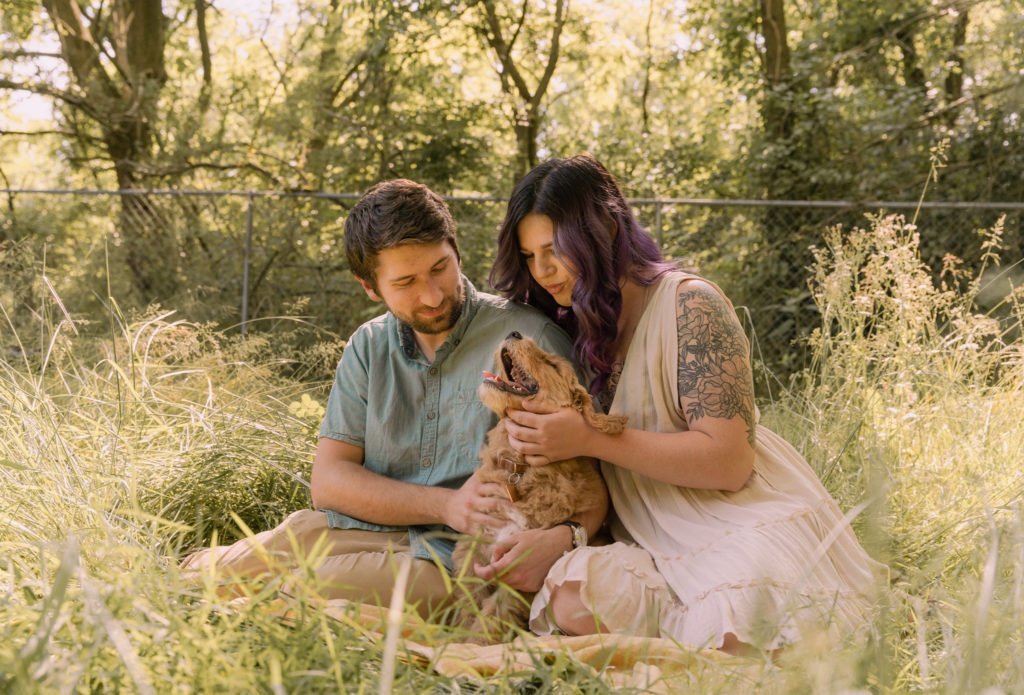 Couple sitting with pup in sunlit field.  Dog Photography tips from PA Family photographer.
